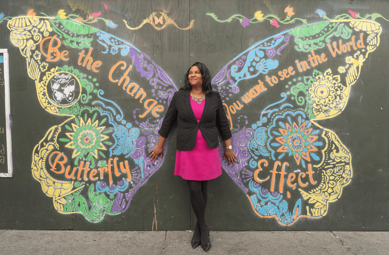 LEOP's Elizabeth McGriff up against a wall that has a butterfly chalk outline, encouraging people to be the change that the want to see and the butterly effect.